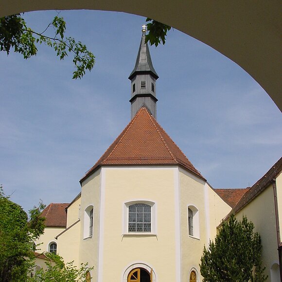 Blich durch den Torbogen auf die Franziskanerkirche mit geöffneter Kirchentür und dem Kirchenvorplatz im Vordergrund.