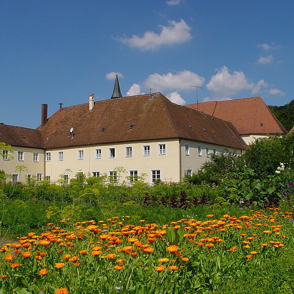 Blumen und Sträucher des Klostergartens, im Hintergrund Klostergebäude.