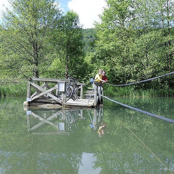 Mit eigener Kraft ziehen Radfahrer auf dem Holzfloß über den Alten Kanal bei Dietfurt.