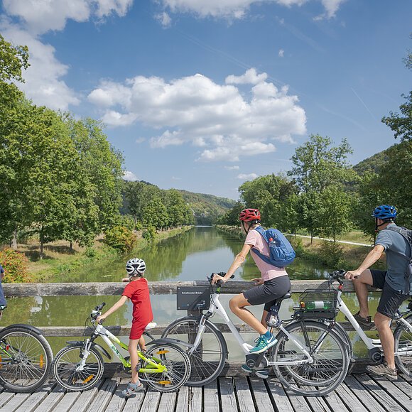 Radfahrer auf dem Altmühltal-Radweg bei Altessing Vier Personen mit Fahrrädern auf einer Holzbrücke mit Blick auf einen Fluss und grüne Landschaft.