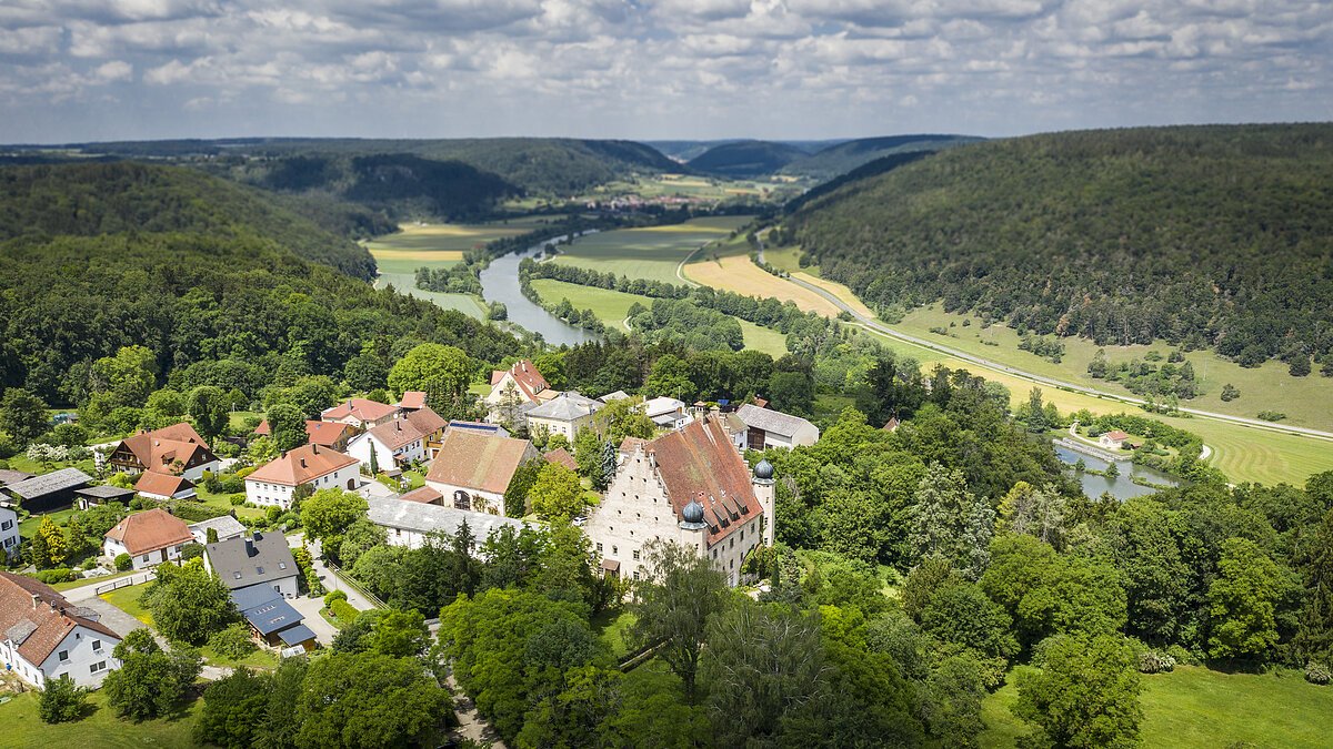 Im Vordergrund ist das Örtchen Obereggersberg mit seiner mächtigen Schlossanlage zu sehen - umgeben von Wald. Im Hintergrund öffnet sich der Blick ins Altmühltal und auf den Main-Donau-Kanal