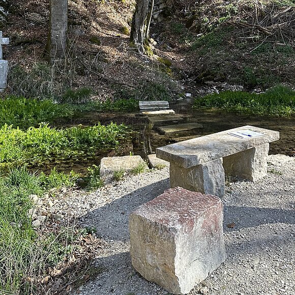 Wald im Hintergrund, Steinkreuz Wasser, Steine im Wasser und Steine als Abgrenzung